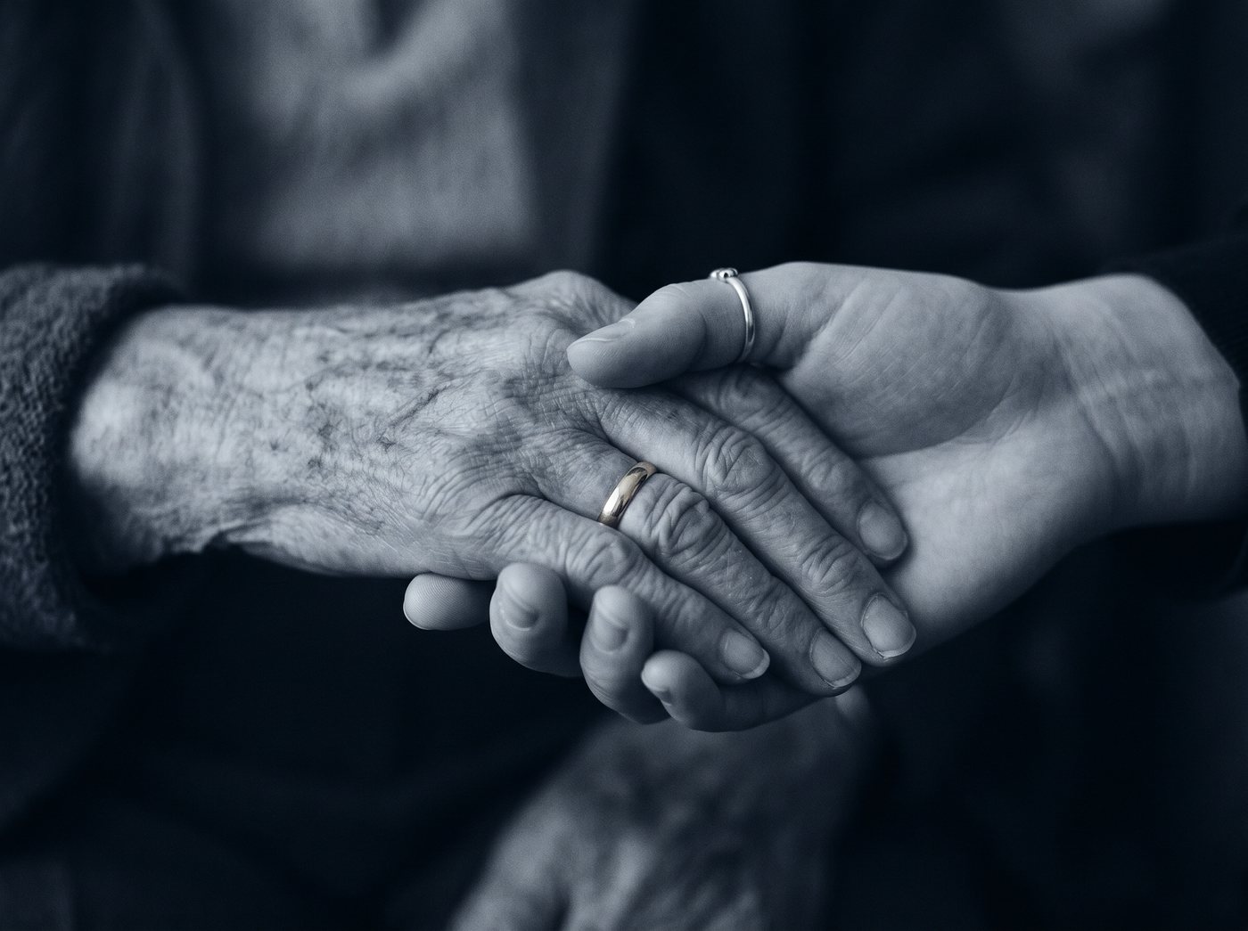 An adult child holding an elderly parent's hand